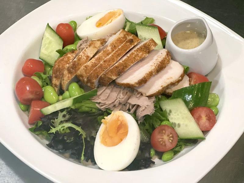 Salad with sliced chicken breast, boiled eggs, tuna, cucumber, cherry tomatoes, edamame beans, and dressing