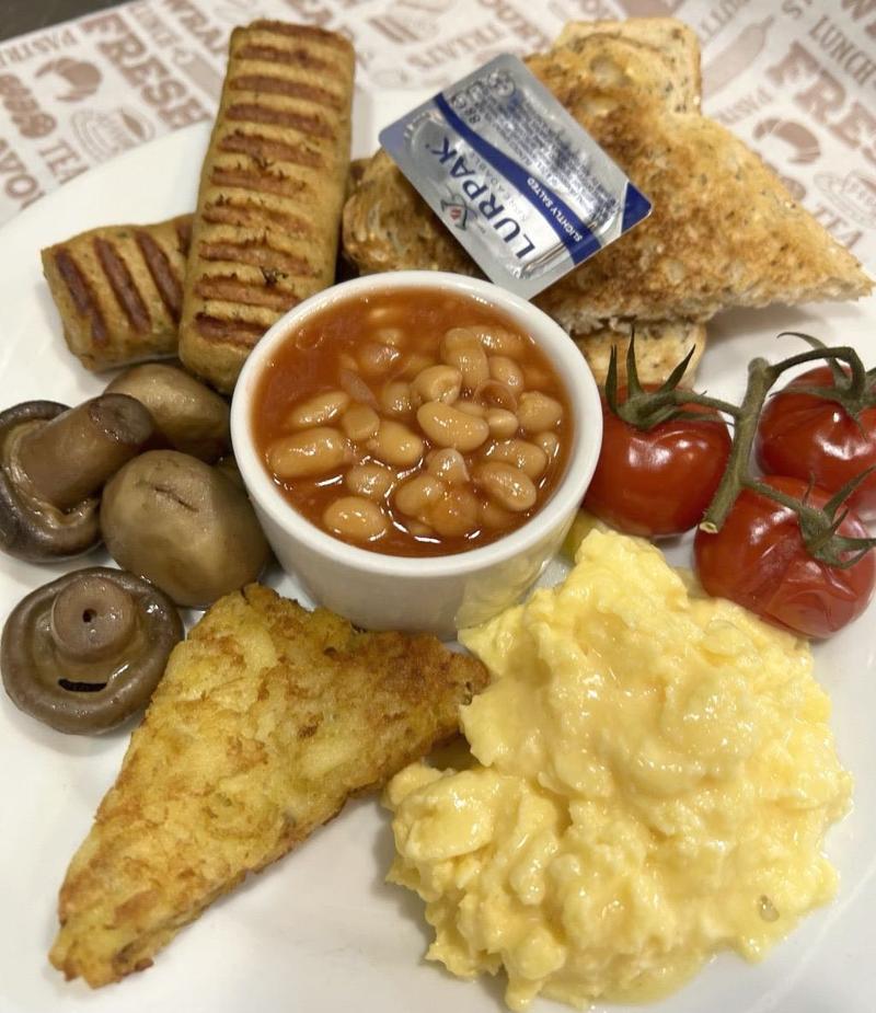 Vegetarian breakfast with scrambled eggs, baked beans, mushrooms, hash brown, grilled tomatoes, toast, and plant-based sausage